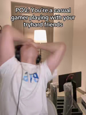 The cover image shows a slightly blurred, medium shot of a person with fair skin, wearing a white t-shirt, headphones, and covering their face with their hands. The person is positioned as if reacting to something, their head is tilted back and their arms are raised around their head as if in frustration or exasperation. The background is an interior, featuring a wall, what appears to be a lamp, and glimpses of computer equipment. Text overlayed on the image reads "POV: You're a casual gamer playing with your tryhard friends". The overall composition and the pose convey a sense of comedic frustration or overwhelm.