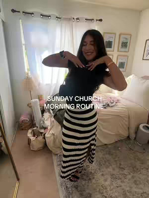 A young woman stands in a bedroom, striking a pose that showcases her attire. She wears a black top paired with a black and white striped skirt. Her arms are raised with her hands near her face. The bedroom has soft lighting. The text "SUNDAY CHURCH MORNING ROUTINE" is overlaid on the image.