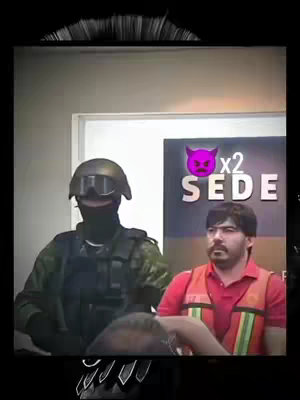 The image shows a man in an orange vest being escorted by a person in tactical gear with a helmet and face covering. The background indicates they are in a government building with a sign that says 'SEDE'.