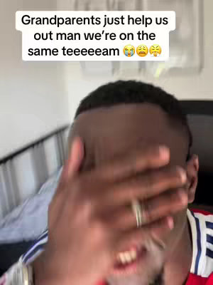 A close-up shot of a Black man covering his face with his hand, revealing only his mouth and part of his eyes. He is smiling. A text overlay at the top reads, 'Grandparents just help us out man we're on the same teeeeeeam' with crying and upset face emojis.