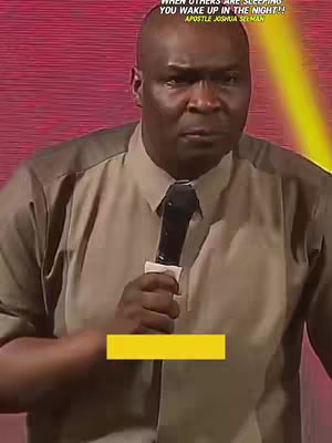 A man with a bald head is holding a microphone, wearing a two-tone collared shirt and a black tie. He has a serious expression. Overlaid on the image, there is white text at the top and a mostly yellow, rectangular highlight near the bottom. The background is blurred in varying shades of red and yellow.