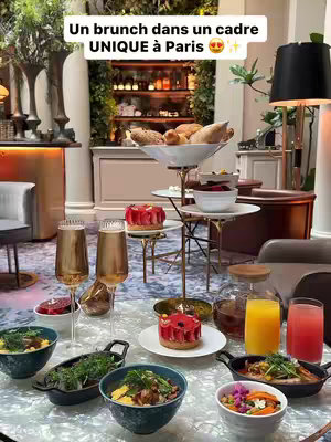 A photo of a brunch table setting, with various dishes of food and drinks, champagne flutes, and a tiered serving stand holding various items. The setting is a luxurious restaurant interior with fancy lighting and decor.