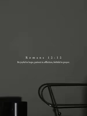 A minimalist, vertical image with a dark gray background. In the center, there is white text that says "Romans 12:12" followed by the verse, "Be joyful in hope, patient in affliction, faithful in prayer." In the foreground, a partially visible black metal chair and a black square are visible.