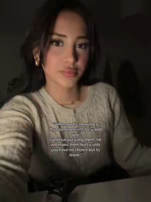 A young woman with dark hair and fair skin is the focus of this selfie-style video cover image. She is positioned in the center, gazing directly at the camera, with soft, warm lighting illuminating her face. The background is dimly lit. Text is overlaid at the bottom, consisting of an inspirational or reflective quote.