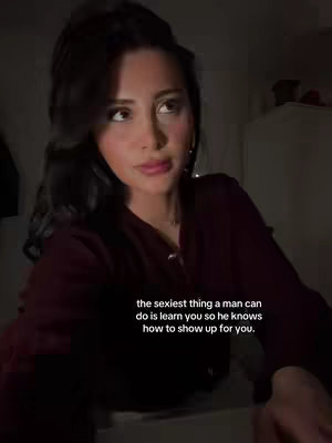 A woman with dark hair in a maroon top is the central focus, lit in a dimly lit room. Text overlayed on the bottom. The woman's gaze is directed upwards thoughtfully, and her expression is contemplative. The background is dark, but there is a hint of a white wardrobe.