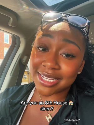 A selfie taken from inside a car, featuring a Black woman with sunglasses resting on her head. She is smiling and looking slightly off-camera, with her expression suggesting a conversational tone. The lighting appears natural, possibly from the sun, and the background includes elements of an urban setting.