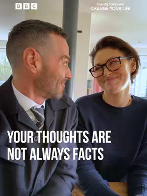 The cover image features two people, a man and a woman, in a medium close-up shot. The man, on the left, is looking at the woman, who is positioned on the right. The man is wearing a dark suit jacket over a white dress shirt, and a striped tie. The woman is wearing glasses and a dark sweater. The background seems to be a domestic setting with elements of white and natural light. Written on the bottom of the image is the text: YOUR THOUGHTS ARE NOT ALWAYS FACTS. There is BBC and Change Your Mind text at the top of the image.