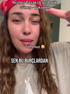 A woman with long brown hair looks directly at the camera. She wears a red bandana. Text overlays are at the top and bottom and an emoji is also present. The background is neutral.