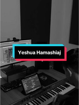 A grayscale image shows a person at a music studio setup. The person is partially visible, seated in front of a keyboard. A computer monitor shows a music production interface. A teal and red text box overlay features the words “Yeshua Hamashiaj” in white text.