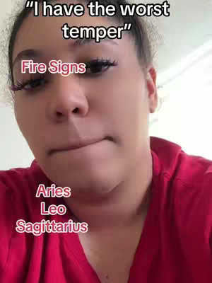 A close-up selfie shows a woman with dark hair pulled back, wearing a red top. Text overlays describe astrological fire signs. The woman has full lips, prominent eyelashes, and slightly furrowed brows.
