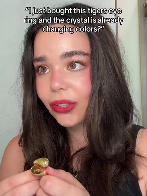 A selfie-style shot of a young woman with dark brown hair and fair skin. She is looking at the camera with a concerned expression and her mouth slightly open. She is wearing a ring with a large, golden stone on her finger. There is a text overlay above her head.