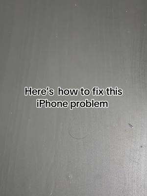 A close-up shot of a grey surface. Centered on the surface is white text that reads, "Here's how to fix this iPhone problem."