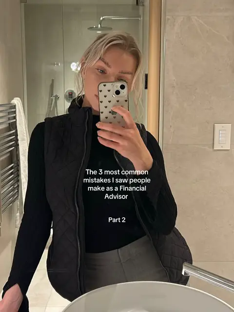 A woman takes a mirror selfie in a bathroom. She's wearing a black quilted vest over a black top and gray pants. Her blonde hair is styled back. She is holding a phone with a black heart design case up to her face. Text overlays the image.
