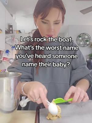 A woman in a gray hoodie is shown using a white spoon to scoop some cookie dough from a green spoon onto the parchment paper on a counter. Above her head is the text "Let's rock the boat. What's the worst name you've heard someone name their baby?"