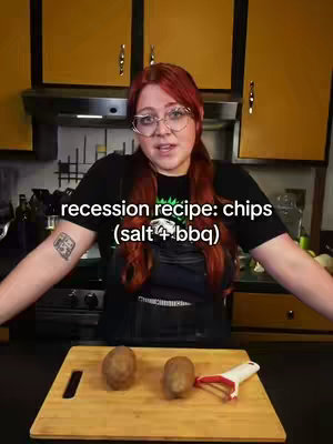 A woman with red hair and glasses stands in a kitchen, arms outstretched. The background shows yellow cabinets. A wooden cutting board with potatoes and a peeler sits in front. Text overlay reads 'recession recipe: chips (salt + bbq)'.
