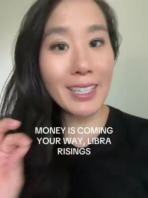 A medium shot features a woman with long, dark hair and a black shirt. The background is a simple light-colored wall. Text overlays on the image read "MONEY IS COMING YOUR WAY, LIBRA RISINGS". The woman is smiling and gesturing with her hand.
