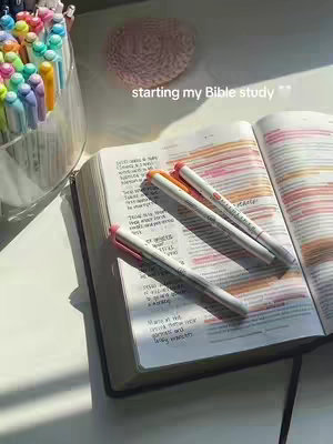 The image shows an open Bible with several colorful pens lying on it, ready for journaling. The open pages reveal highlighted passages.