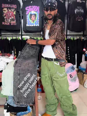 A man stands in a clothing store, holding a pair of jeans, with apparel racks visible in the background.