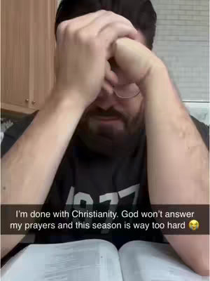 A person is shown with their hands covering their face, suggesting distress or contemplation. They are wearing glasses and a dark t-shirt. A book is open in front of them.