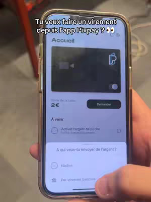 A hand holding a smartphone displaying the Pixpay app on the screen. The app interface shows a black digital card with a balance of 2€, and a 'Demander' button. The background is blurred, but appears to be of an indoor setting.