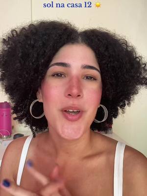 A woman with curly dark hair is centered. She has fair skin, blush, and is wearing a white tank top and hoop earrings. Above her, text floats; in the background, a pink bottle of what may be lotion is visible.