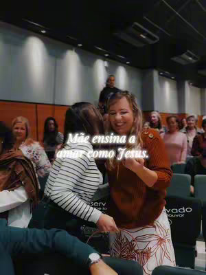 The image captures a moment within a church setting, featuring two women embracing. The woman on the right has blonde hair. The background includes rows of seated individuals, likely a congregation, and the interior has warm lighting.