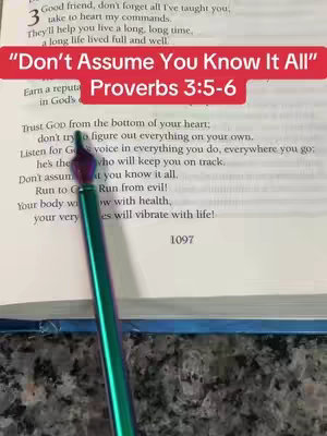 The image shows an open book with highlighted text and an overlay across the top. A pen is positioned diagonally across the pages, pointing towards the text. The background has a marble texture.