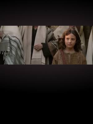 The cover image is a scene from a film. It shows a young boy in a brown robe, possibly portraying a historical or religious figure; he is the central element. To the left and right of him are partially visible figures, likely bystanders or those in the young boy's company, dressed in modest attire. The boy looks directly at the viewer, appearing contemplative and composed. The lighting is soft, and the color palette is muted, with tones of brown, beige, and gray. The composition is simple, focusing the viewer's attention on the boy. The background is blurred, directing focus towards the main subject.