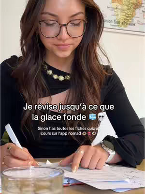 A young woman with long brown hair and glasses is sitting at a desk working. She is wearing a black top and a necklace. On the desk are papers and a pen, and the text bubble overlays read in french, encouraging studying for exams. There is a map on the background.