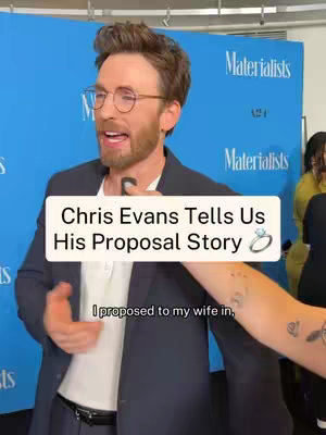 The image shows Chris Evans in an interview setting, likely on a red carpet. He wears glasses and a dark blazer. A text overlay indicates the video is about his proposal story.