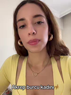 A woman with long brown hair, gold hoop earrings, and a yellow top. She is looking at the camera with a neutral expression and her lip slightly pursed as though in though. There is text overlaid on the image, and a blurred background.