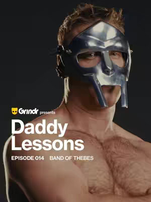 A shirtless man wearing a metallic mask reminiscent of an ancient gladiator/roman soldier. The man has short, light-colored hair, and is looking towards the camera. The background is a solid, dark gray color, which highlights the man. Text overlays with the words "Daddy Lessons" in large white fonts and Grindr branding.