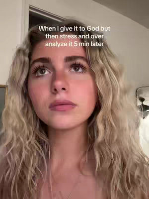 A medium shot shows a young woman looking upward with a contemplative expression. She has long, wavy blonde hair and is positioned against a soft background with a hint of a door and a reflective surface. The lighting is natural, and her gaze is the focal point.