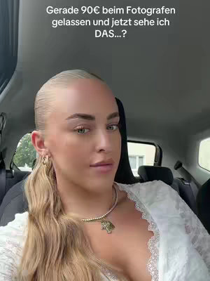 A selfie taken from inside a car, featuring a fair-skinned woman with blonde hair pulled back. She is wearing a white, lacy top and a necklace with a pendant. Text overlayed on the image reads in German, 'Gerade 90€ beim Fotografen gelassen und jetzt sehe ich DAS...?'. The background shows details of the car's interior and a glimpse of an outside window.