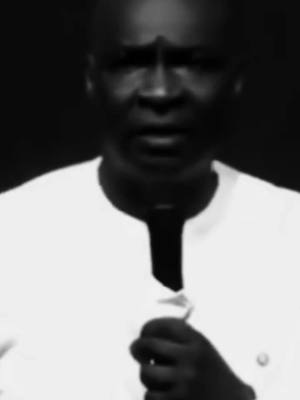 A grayscale image featuring a man with a bald head, dressed in a white collared shirt. His face is the primary focus, suggesting a close-up, and he appears to be speaking, with his mouth slightly open. The background is a dark, solid color, highlighting the man's features and attire. The composition is simple, focusing solely on the individual and the impression of a message or statement.