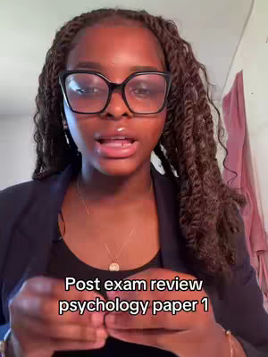 The cover image is a selfie of a young woman with dark skin and long, twisted braids. She is wearing large, black-framed glasses, a black shirt with a blazer, and a delicate necklace. The background is out of focus, with hints of a wall and possibly some clothing. The text overlay at the bottom says 'Post exam review psychology paper 1'. The overall composition is a medium close-up, with the woman's face centered and her hands slightly visible.