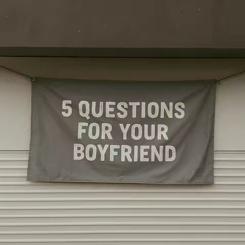 A grey banner hangs against a background of white siding. The banner features bold, white text reading "5 QUESTIONS FOR YOUR BOYFRIEND."