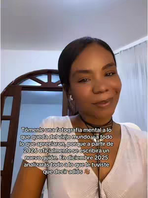 A selfie style shot. Portrait, front face of a woman with dark hair and light skin. Soft lighting. She is in a white top and a black choker necklace. Behind her is a wooden door and white walls.