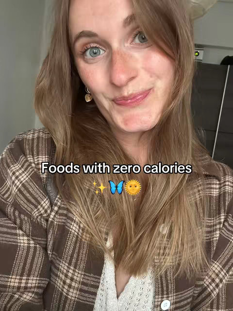 A woman with long blonde hair is in a selfie shot. The overlay text reads "Foods with zero calories" with a sparkle, a butterfly, and a sun emoji. The woman is wearing a brown plaid shirt over a white shirt.
