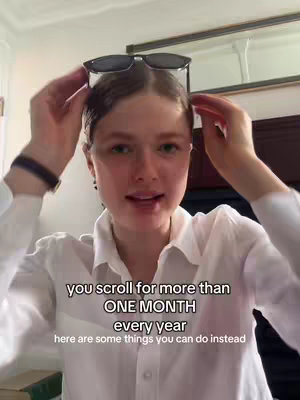 A woman is holding sunglasses on top of her head and is looking at the camera. Text over the image says: "you scroll for more than, ONE MONTH, every year, here are some things you can do instead". The background appears to be indoors, with a window and a dark framed picture visible.
