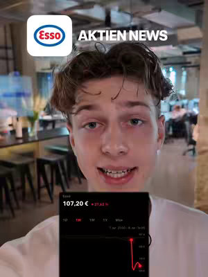 A young man with short brown hair is centered in the frame, smiling and speaking directly to the viewer. Behind him, a blurred background suggests an office or public space. The man holds a phone displaying a stock chart showing a sharp decline. The image is framed in a vertical format, typical of a mobile screen.