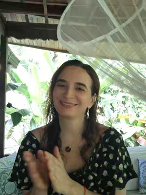 The cover image shows a woman in a black and white floral top. She is smiling and clapping her hands, with a blurred background of greenery and a white canopy.