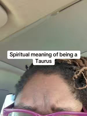The cover image shows a close-up of a person's forehead, eyes, and part of their hair. The person is wearing glasses with pink-colored frames. The text overlay is displayed within a white bar that reads: 'Spiritual meaning of being a Taurus'. The background is a blurry view of the inside of a vehicle, likely a car.