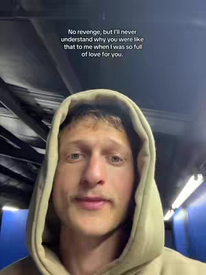 A selfie-style video cover featuring a young man wearing a beige hoodie, with text overlayed. The setting appears to be indoors within a dark room. The man is centered in the frame with the text at the top. The man has short, light-brown hair and a light-colored mustache. Shadows and darker tones contrast with the subject's face.