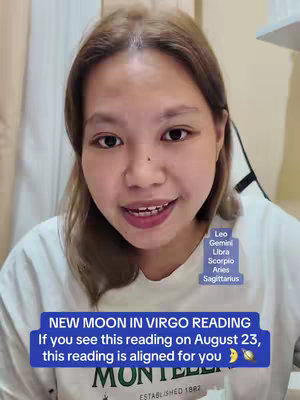 A selfie-style video cover featuring a light-skinned woman with brown hair smiling directly at the camera. She's wearing a white t-shirt and the background suggests an indoor setting, possibly a room. Overlayed text and graphics include astrological signs and a text callout related to readings aligned with a specific date for the new moon in Virgo.