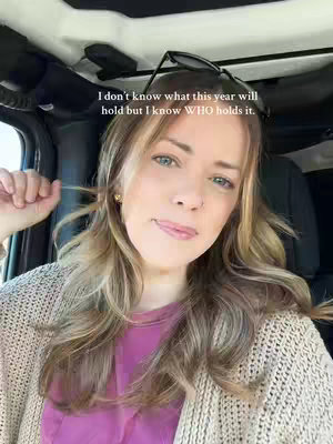 A woman with long blonde hair is seated in a car, looking directly at the camera with a slight smile. Text overlayed on the image reads: 'I don't know what this year will hold but I know WHO holds it.' The background is softly blurred, featuring the car's interior.
