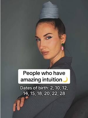 A woman with fair skin and dark hair gazes intently at the camera, her head tilted slightly. She wears a gray top and has a folded fabric accessory on her head. Text on the image suggests the video is about intuition and birth dates.