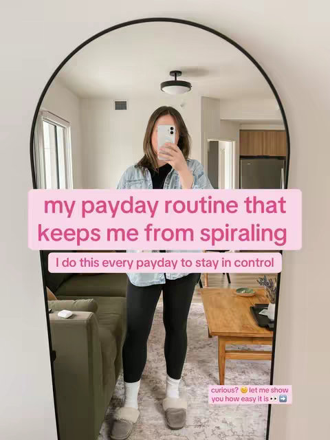 A woman stands in a room, reflected in a large, arched-top mirror. She's holding a phone up near her face. Text overlays on the mirror frame read "my payday routine that keeps me from spiraling".