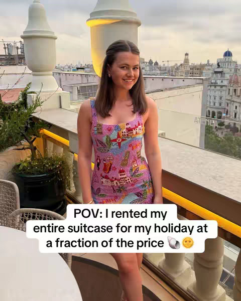 A woman in a colorful dress stands on a balcony overlooking a cityscape. The image has a warm color palette, focusing on the woman and the scenery behind her.