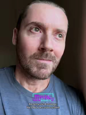 A close-up shot of a man with light skin, a trimmed beard, and light-colored eyes. He is looking slightly to the side with a subtle smile. Overlaying the image is a lower-third graphic with the text "Mystic Rebels" and a caption below that reads "Alchemystic Astrology: the ONLY accurate system."
